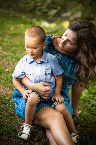 Νεαρή μητέρα κάθεται στο γρασίδι με τον μικρό γιο της — Φωτογραφία Αρχείου