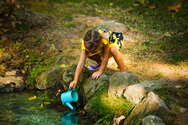 Nettes kleines Mädchen schöpft Wasser in Eimer aus Bach — Stockfoto
