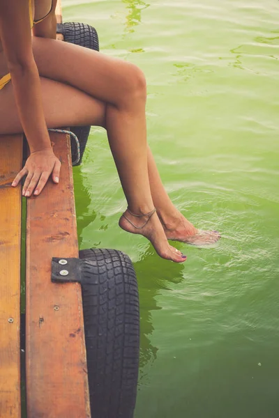 Woman sit on wooden dock cooling feet in clear water — Stock Photo, Image