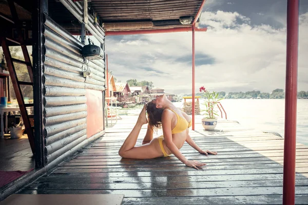 Cvičím jógu mladá žena v bikinách na dřevěné řeka raft — Stock fotografie