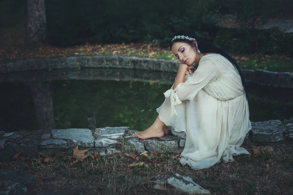 Giovane donna in abito romantico e decorazione dei capelli sedersi da stagno — Foto Stock