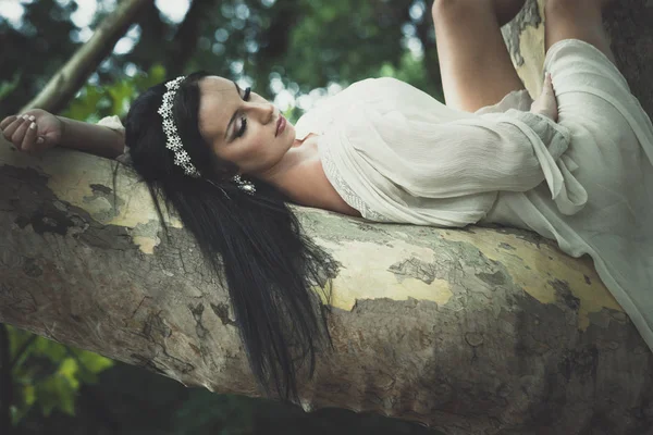 Mooie jonge vrouw in romantische jurk leugen op boom in park — Stockfoto