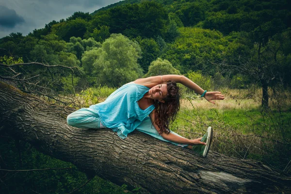 Jonge vrouw praktijk yoga buiten op enorme boom viel op de berg — Stockfoto