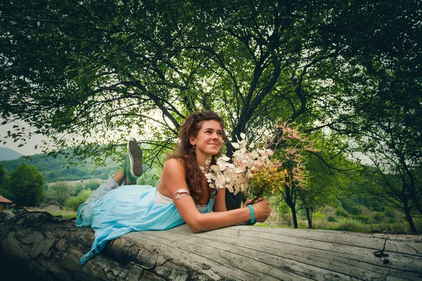 Heureux jeune femme posant sur énorme arbre avec un bouquet de sauvage fl — Photo