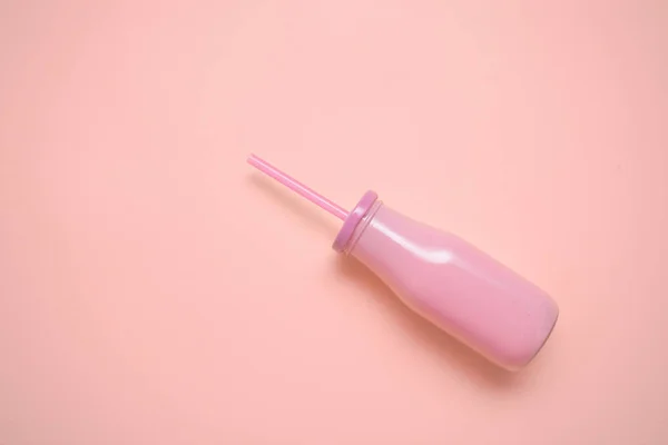 pink glass bottle with straw on pastel pink paper background