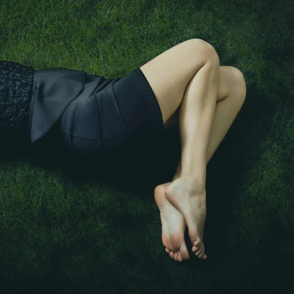 Mulher descalça em vestido preto mentira na grama — Fotografia de Stock