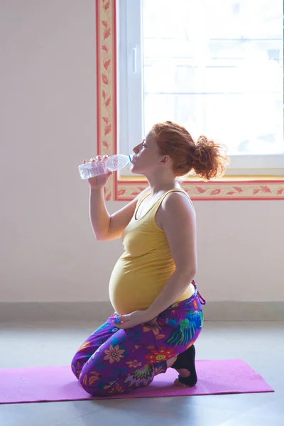 Rött huvud gravid ung kvinna på yoga klass dricksvatten — Stockfoto