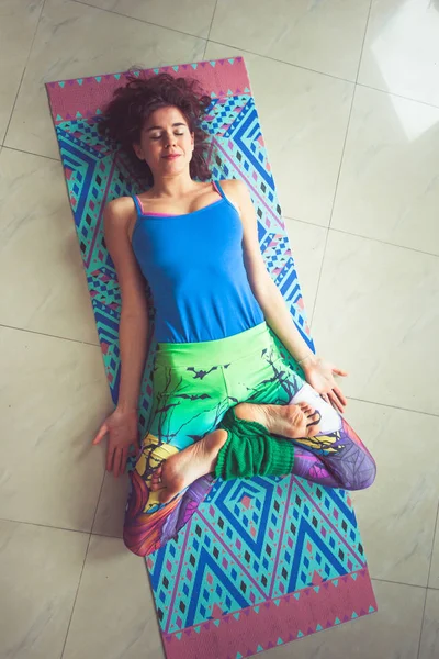Ung kvinna liggande på matta med ben i lotusställning inomhus skott — Stockfoto