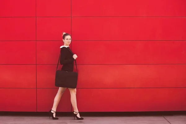 Jovem mulher de negócios elegante andar na frente parede vermelha na cidade — Fotografia de Stock