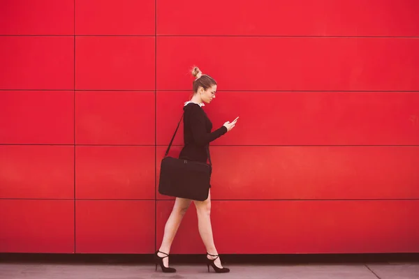 Jovem mulher de negócios elegante andar na frente parede vermelha na cidade — Fotografia de Stock