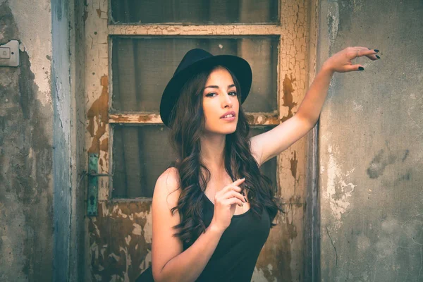 Jeune femme de mode avec chapeau debout devant vieille maison abandonnée — Photo