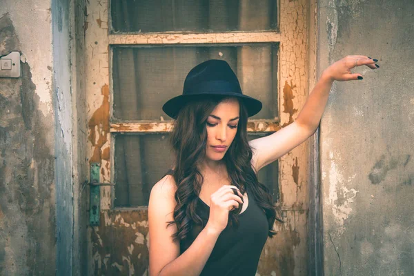 Jeune femme de mode avec chapeau debout devant vieille maison abandonnée — Photo