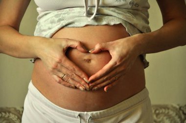 Hamile kadın, ellerini bebeğin karnındaki kalp gibi katladı.