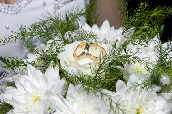 Gold wedding rings are on a wedding bouquet in the hands of the bride