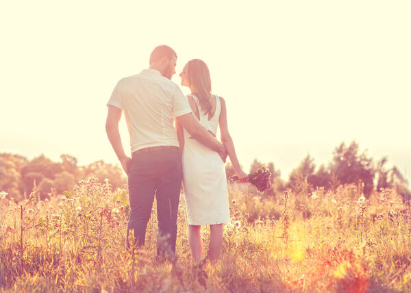 Молодая пара влюбленных гуляет по осеннему парку, держась за руки.
