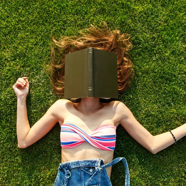 Flicka liggande på gräset som täcker ansiktet av boken, conce — Stockfoto