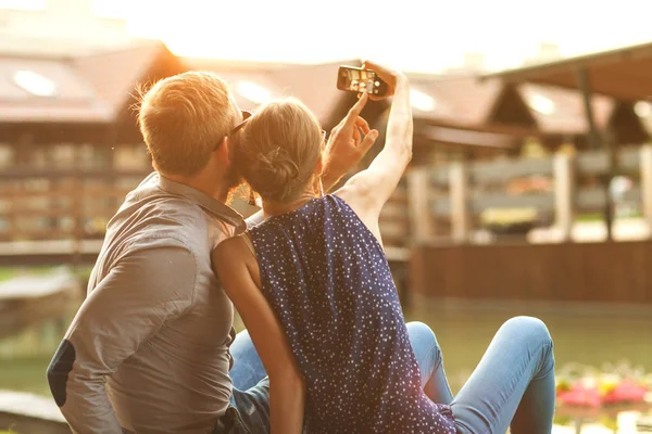 Para zakochanych siedzi w parku o zachodzie słońca sprawia, że selfie — Zdjęcie stockowe