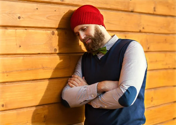 Hipster-Typ lächelt in roter Mütze, Hintergrund hölzern, Weihnachten — Stockfoto