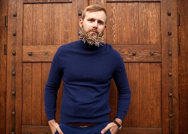 Mode hipster kille står nära en trädörr tandpetare i hans skägg, hat, ilska, förakt, svek, girighet. — Stockfoto
