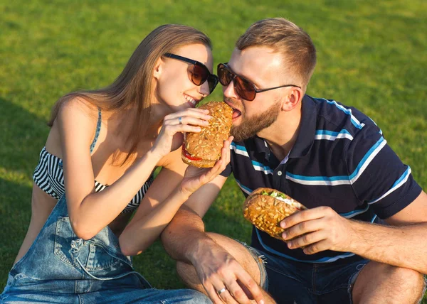 Casal sentado na grama no parque e comer sanduíches sm — Fotografia de Stock