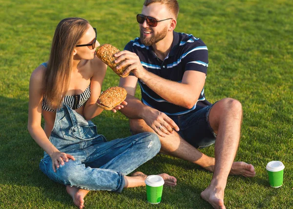 Pareja sentado en la hierba en el parque y comer sándwiches sm — Foto de Stock