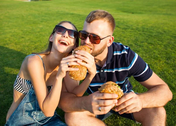 Couple in love sitting on the grass in the park and eating sandw — Stock Photo, Image