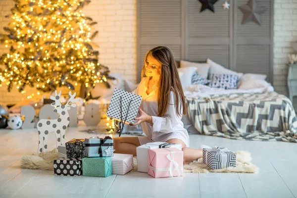 Dziewczyna, w domu na Boże Narodzenie, patrząc na prezenty pod tre Boże Narodzenie — Zdjęcie stockowe