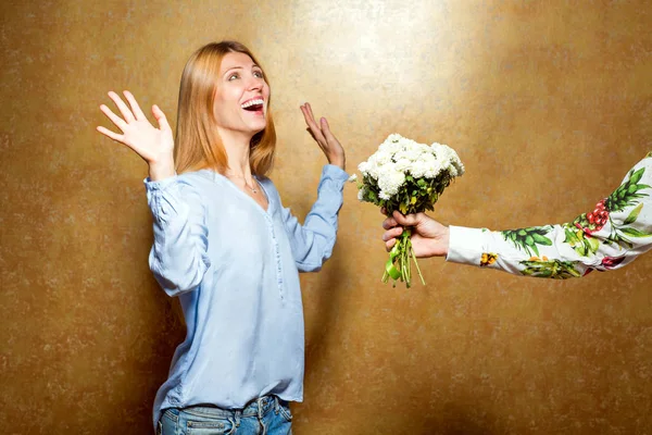Girl giving flowers in the studio on a gold background, the conc — Stock Photo, Image