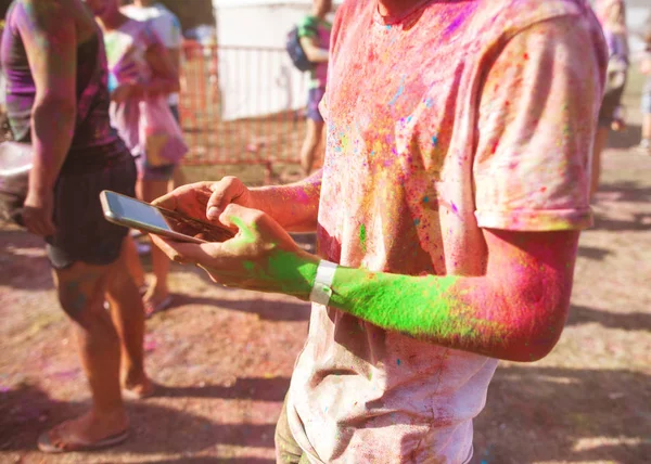 Guy celebrates the festival of holi, holds the phone in his hand — Stock Photo, Image