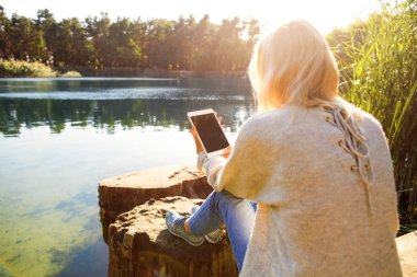 Kız bir göl sonbahar bir Parkı bir tablet tutar
