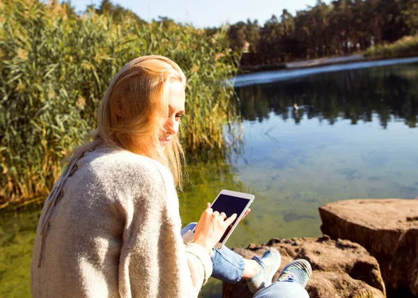 Mädchen in einem Park in der Nähe eines Sees hält ein Tablet in der Hand — Stockfoto