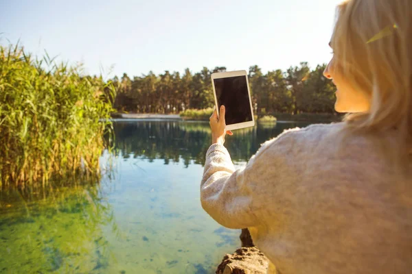 Girl in an autumn park near a lake holds a tablet — Stock Photo, Image