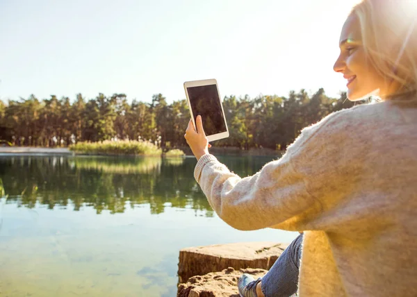 Kız bir göl sonbahar bir Parkı bir tablet tutar