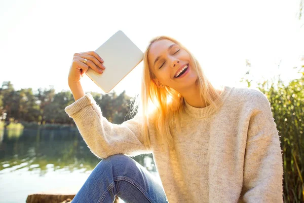 Dívka v podzimním parku nedaleko jezera drží tablet — Stock fotografie