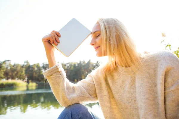 Menina em um parque de outono perto de um lago detém um tablet — Fotografia de Stock