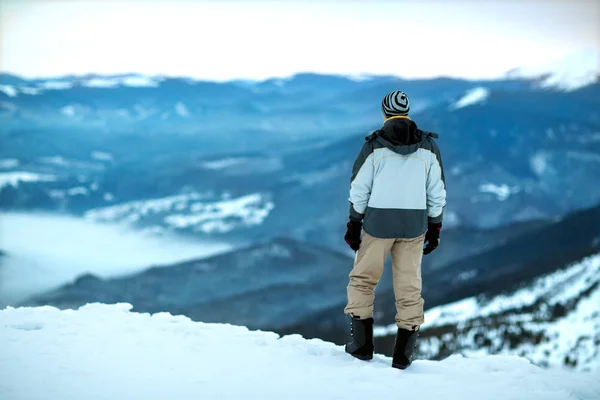 De man staat op de top van een besneeuwde berg op zoek naar de — Stockfoto