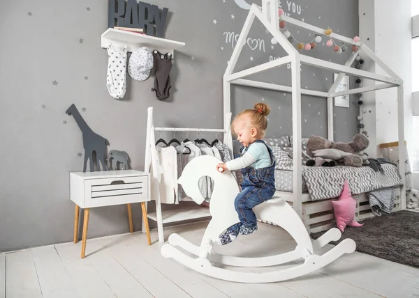 Één jaar oud meisje speelt in de buurt van in de kamer met een paard van speelgoed, schaatsen — Stockfoto