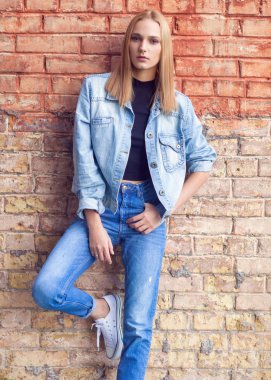 tuğla duvar denim ve spor ayakkabı yakın duran kız moda. Vogue stili