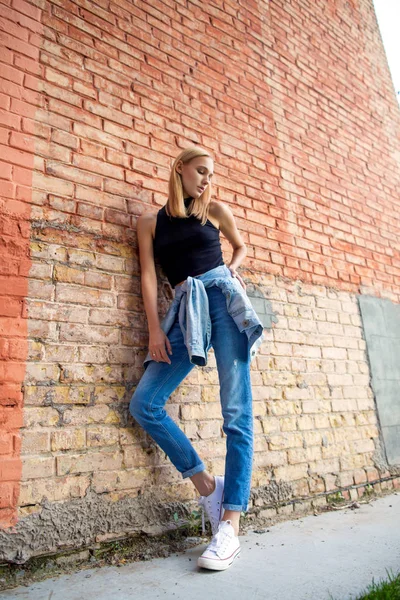 Modemädchen, das in Jeans und Turnschuhen in der Nähe der Mauer steht. Modestil — Stockfoto