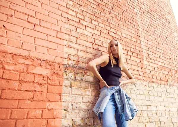 Modemädchen, das in Jeans und Turnschuhen in der Nähe der Mauer steht. Modestil — Stockfoto
