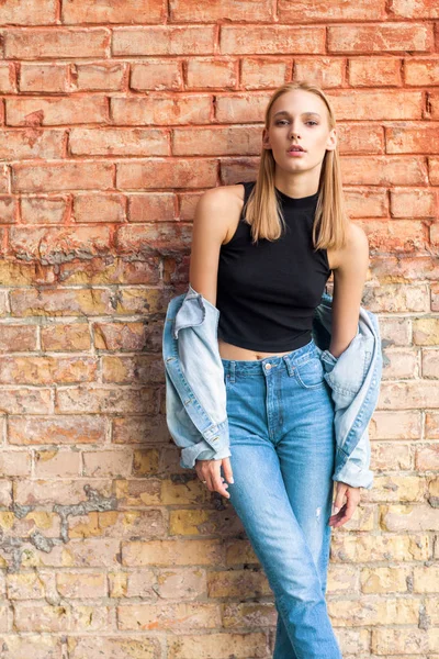 Девушка из моды, стоящая возле кирпичной стены в джинсах и кроссовках. Vogue Style — стоковое фото