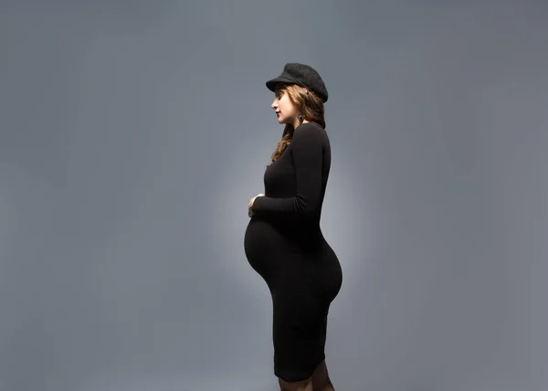 Beautiful fashionable girl pregnant in studio stands posing — Stock Photo, Image