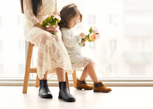 Matka a dcera se bavit, stojící poblíž obrovské okno, dcera dává jí květiny matce její matky den. — Stock fotografie