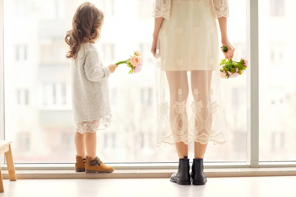 Madre e hija se divierten de pie cerca de una enorme ventana, la hija le da flores a su madre en el día de su madre . —  Fotos de Stock