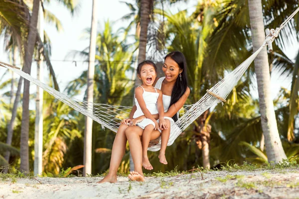 Asiático feliz madre con su hija sentado en un hamaca en la orilla de un tropical playa. Día de las madres . —  Fotos de Stock