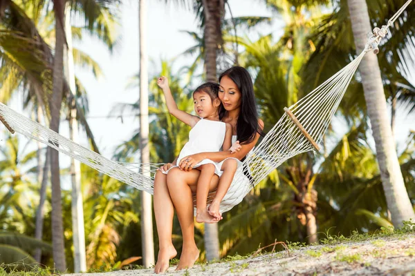 Asiático feliz madre con su hija sentado en un hamaca en la orilla de un tropical playa. Día de las madres . —  Fotos de Stock