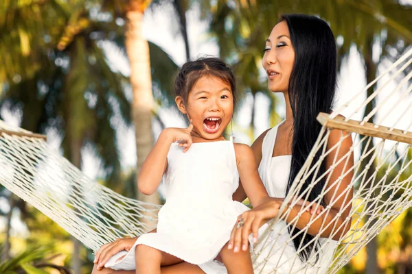 Asiático feliz madre con su hija sentado en un hamaca en la orilla de un tropical playa. Día de las madres . —  Fotos de Stock