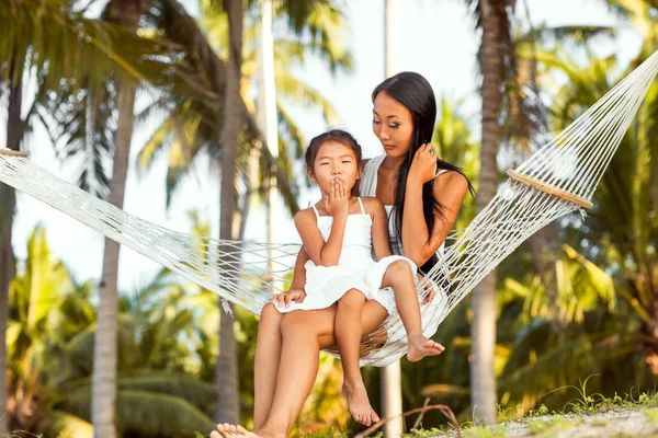 Tropikal bir plaj kıyısında bir hamakta oturmuş kızıyla birlikte Asya mutlu anne. Anneler günü. — Stok fotoğraf