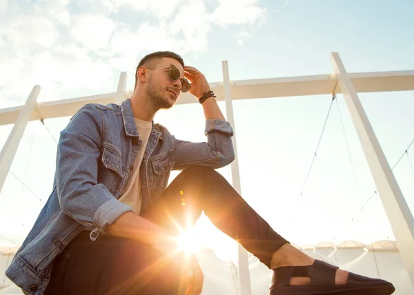 Módní člověk sedí u západu slunce pózuje v sluneční brýle — Stock fotografie