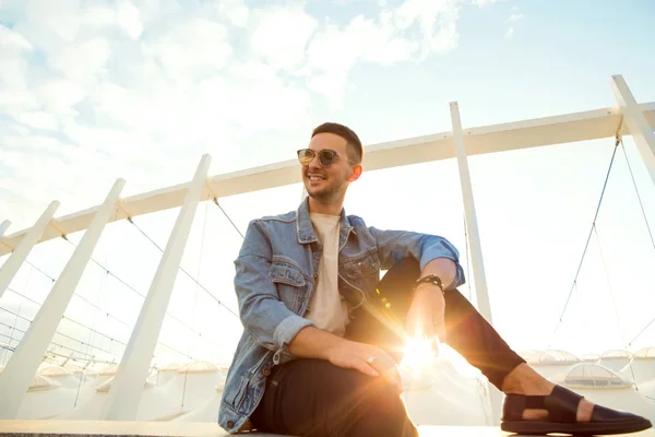 Homme de la mode assis au coucher du soleil posant dans des lunettes de soleil — Photo